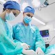 Arzt und Ärztin stehen in Operationssaal und führen Operation an einem Patienten durch
