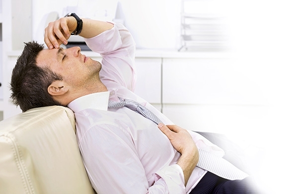 Mann sitzt zuhause auf Sofa und greift sich mit Hand an die Stirn aufgrund von Kopfschmerzen