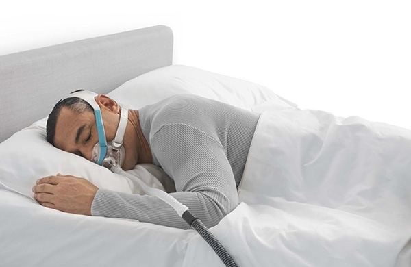 Mann liegt mit Evora Maske zuhause im Bett und schläft ruhig und angenehm auf dem Bauch