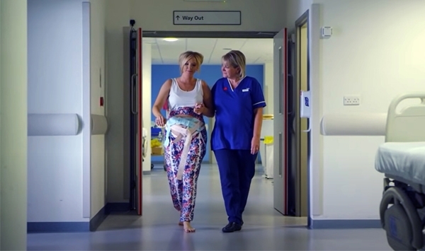 Hochschwangere Frau mit Überwachungs-Pods am Bauch spaziert mit Pflegerin durch Krankenhausflur