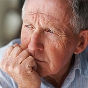 Älterer Mann sitzt zuhause und blickt traurig in die Ferne