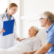 Ärztin steht neben Patientin im Pflegebett, rechts ein Angehöriger