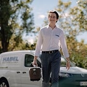HABEL Mitarbeiter mit Sauerstoffkonzentrator in der Hand geht über die Straße und lächelt