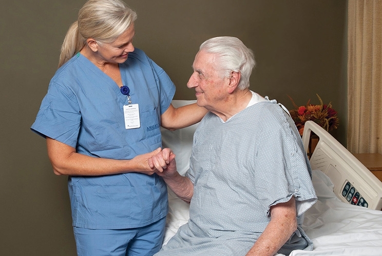Pflegerin hält Hand eines älteren Patienten der aufrecht im Krankenhausbett sitzt