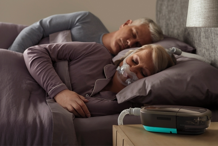 Patientin schläft in ihrem Bett mit Beatmungsmaske, auf dem Nachttisch die DreamStation 2