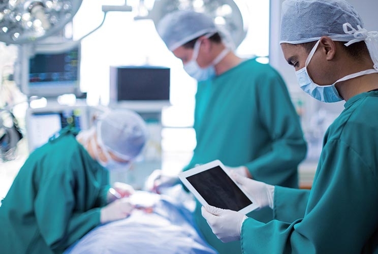 Arzt steht mit Monitor in der Hand am Patientenbett während eine Bronchoskopie durchgeführt wird