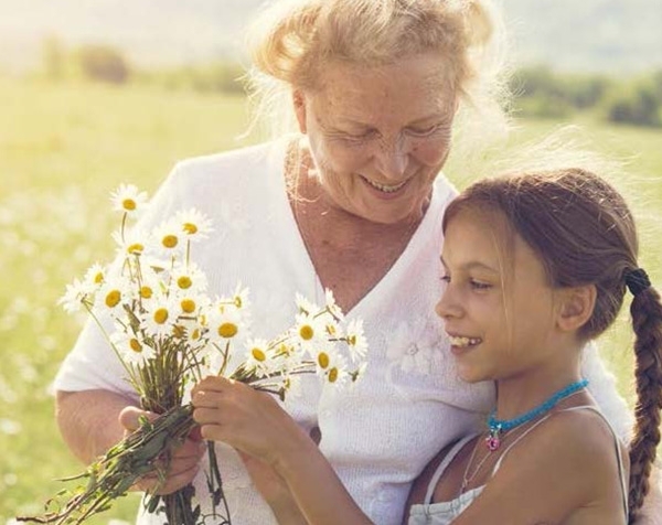 Großmutter steht mit Enkel im Feld mit einem Strauß Blumen in der Hand und beide lächeln