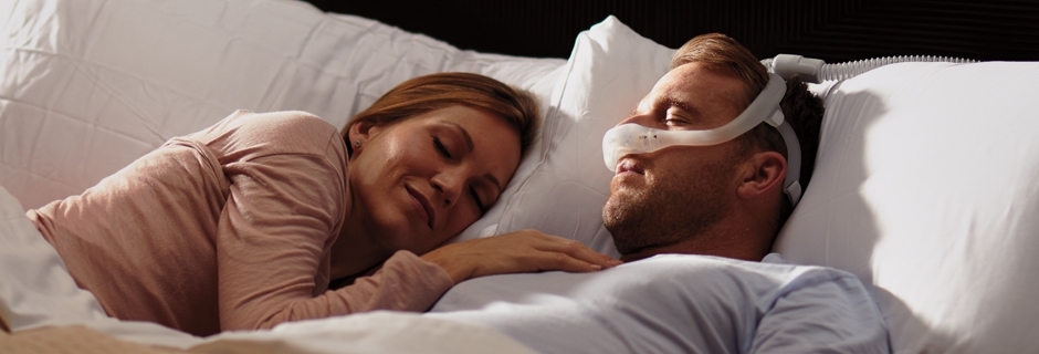 Patient schläft mit Beatmungsmaske, neben ihm schläft Frau