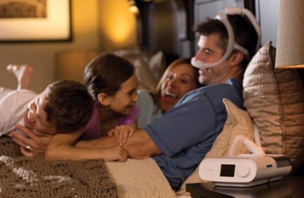 Eltern kuscheln mit ihren zwei kleinen Kindert im Bett, auf dem Nachtkästchen steht die REMstar DreamStation AutoCPAP