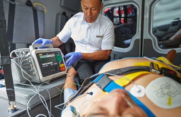 Der Efficia DFM100 in einem Krankenwagen, im Vordergrund ein liegender Patient, im Hintergrund ein Sanitäter
