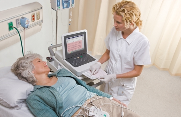 Patientin im Pflegebett, daneben Pflegerin mit PageWriter TC30