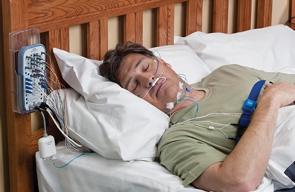 Mann liegt in Schlaflabor an Schlafanalysegerät angeschlossen