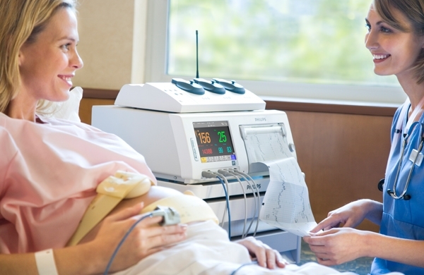 Eine Pflegerin und eine hochschwangere Patientin lächeln sich an, im Hintergrund das Farbdisplay des Avalon FM40