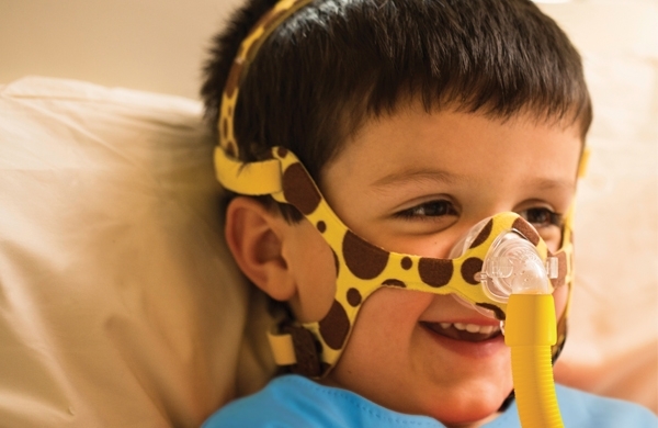 Ein fröhliches Kleinkind im Patientenbett trägt die Nasenmaske PN841