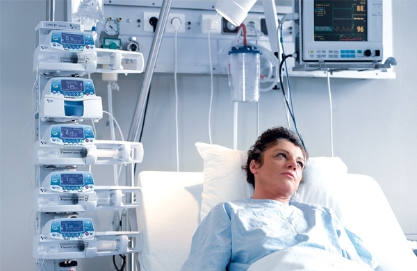 Mehrere Agilia SP PCA-Geräte im Haltesystem gestapelt, daneben eine Patientin im Pflegebett