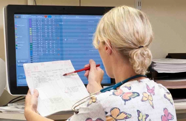 Pflegerin vor einem PC-Bildschirm, der in Echtzeit  die Statusanzeige aller Patienten anzeigt