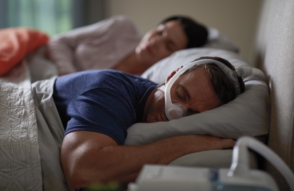 Paar schläft im Bett, Mann liegt auf seinem Bauch und trägt die DreamWisp Maske