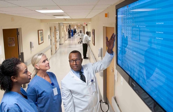 Krankenhauspersonal vor einem großen Bildschirm, der in Echtzeit  die Statusanzeige aller Patienten anzeigt