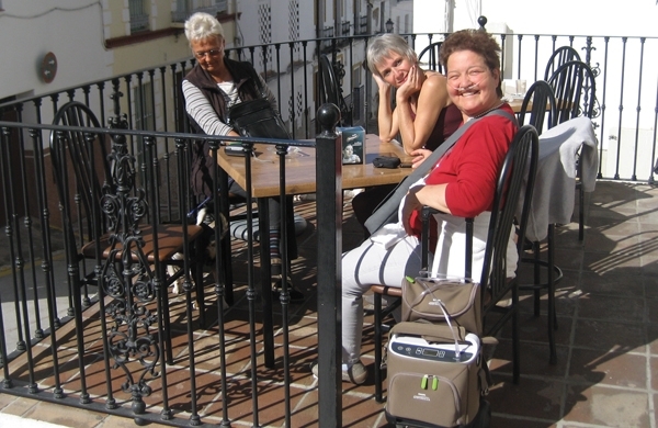 Frau Kramreiter sitzt mit ihrem Gatten und ihrer Cousine draußen an einem Tisch und genießt die Sonne