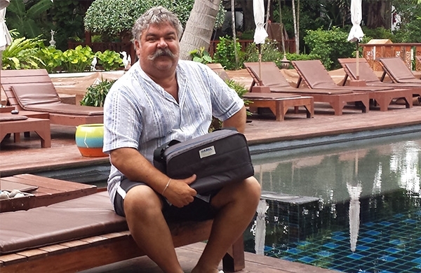 Mann sitzt im Urlaub auf einer Liege beim Pool und lächelt mit DreamStation Reisetasche in der Hand in die Kamera