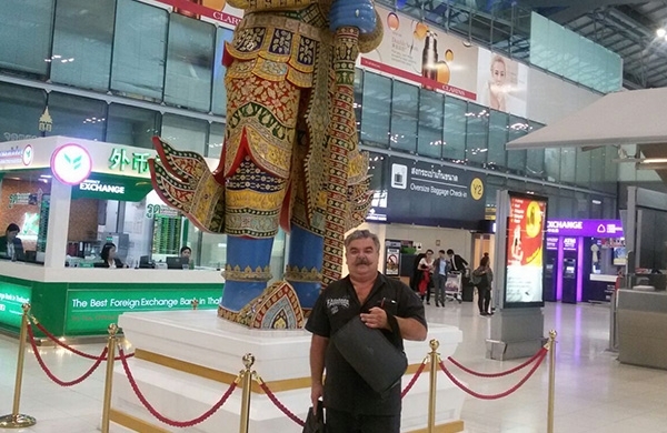 Mann steht mit CPAP Reisetasche in der Hand am Flughafen vor einer Statue