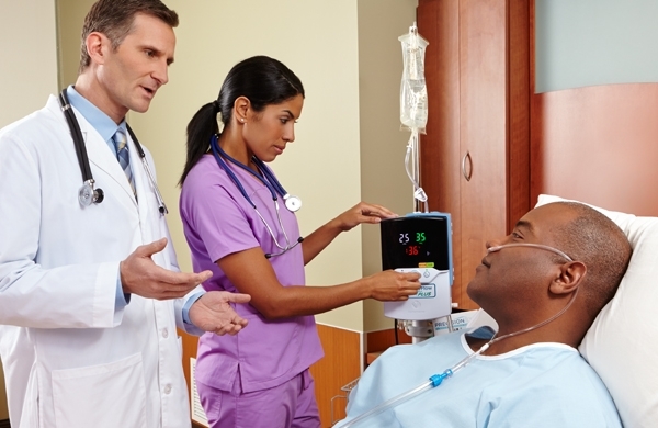 Patient im Pflegebett, neben ihm Arzt und Pflegerin, das Precision Flow Hi-VNI High-Flow Gerät in Verwendung