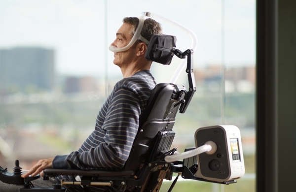 Patient sitzt in einem Rollstuhl und blickt aus einer Fensterfront, der Trilogy Evo ist auf dem Rollstuhl befestigt 