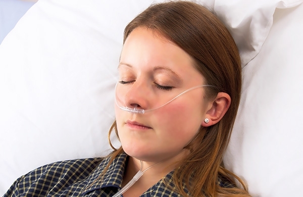 Patientin liegt im Krankenbett mit den Augen geschlossen mit Sauerstoffbrille