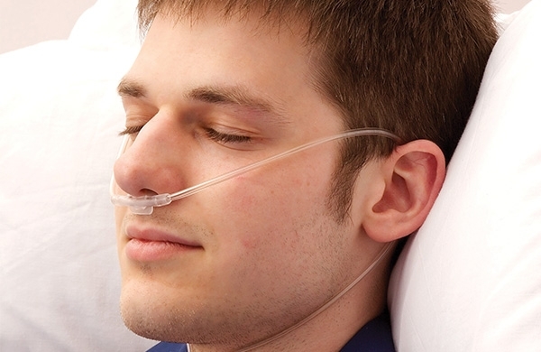 Patient liegt in Bett mit Sauerstoffbrille und Augen geschlossen