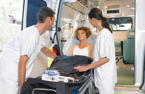Pfleger schieben eine Patientin im Pflegebett in einen Rettungswagen