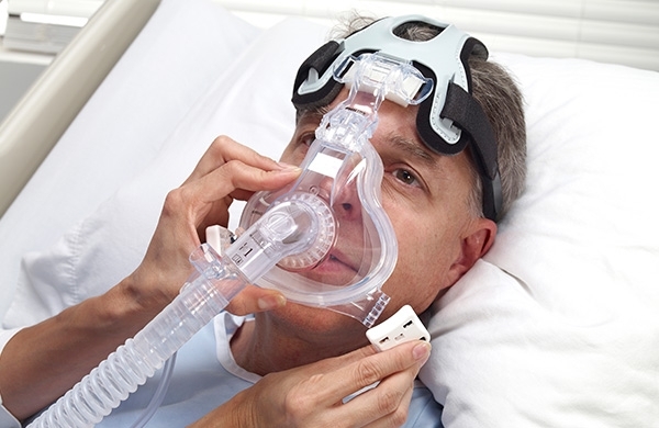 Patient bekommt Maske angepasst, liegt in Krankenhausbett und blickt in die Ferne