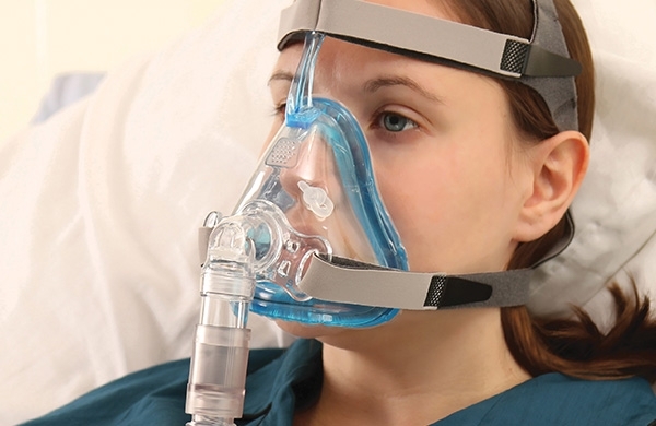 Patientin mit Maske in Krankenhausbett blickt in die Ferne
