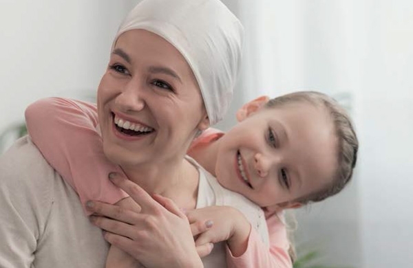 Krebspatientin wird von Kind umarmt und beide lächeln