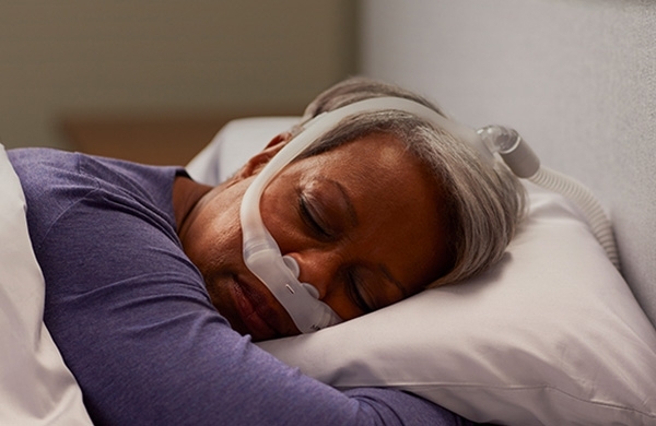 Patientin liegt mit DreamWear Nasenolivenmaske im Bett auf dem Bauch und schläft
