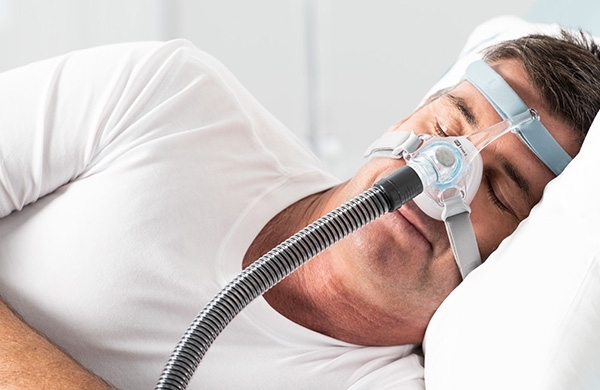 CPAP Patient liegt mit Eson 2 Nasenmaske seitlich im Bett und schläft