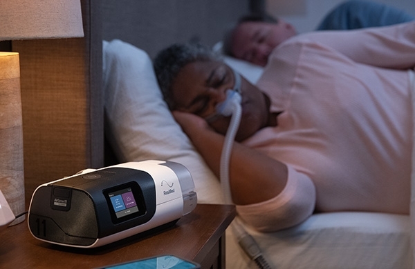 AirSense steht auf dem Nachttisch und CPAP Anwenderin schläft mit CPAP Maske im Bett