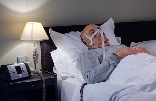 CPAP Anwender liegt mit Nasenmaske im Bett und schläft und wird mit Lumis beatmet