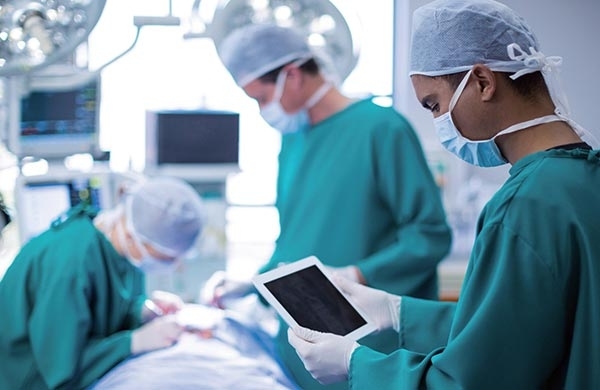 Arzt steht mit Monitor in der Hand am Patientenbett während eine Bronchoskopie durchgeführt wird