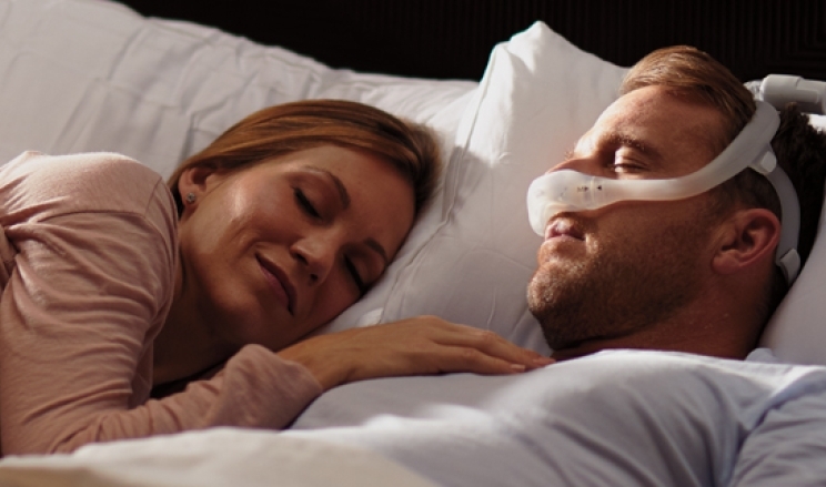 Patient schläft mit Beatmungsmaske, neben ihm schläft Frau