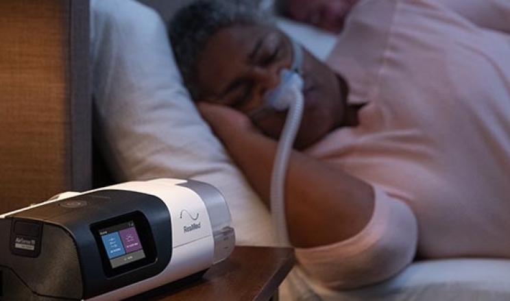 Frau schläft mit Maske im Bett, CPAP Gerät steht auf Nachttisch